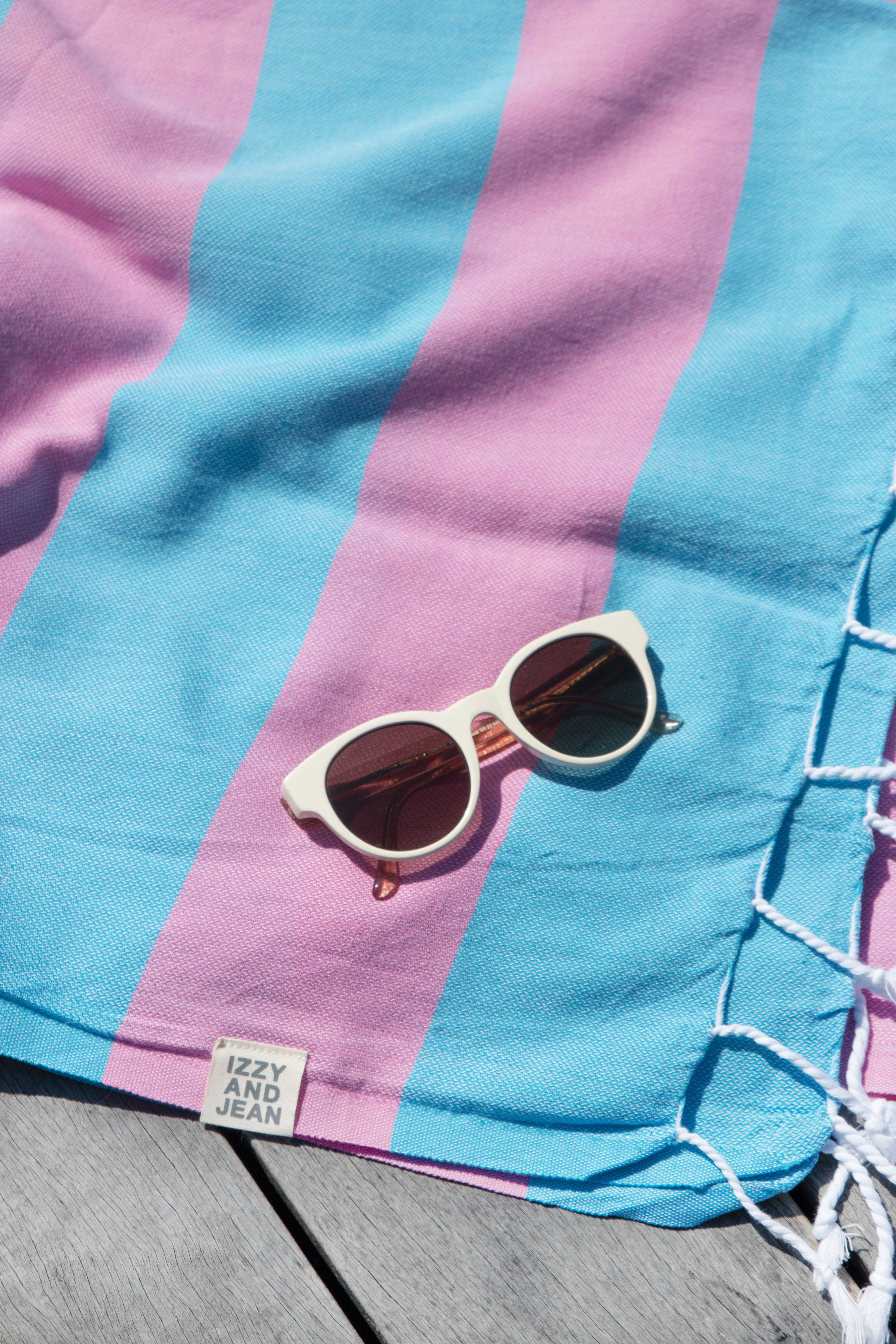 The Santorini Hot pink and marine Turkish towel with white sunglasses on top.