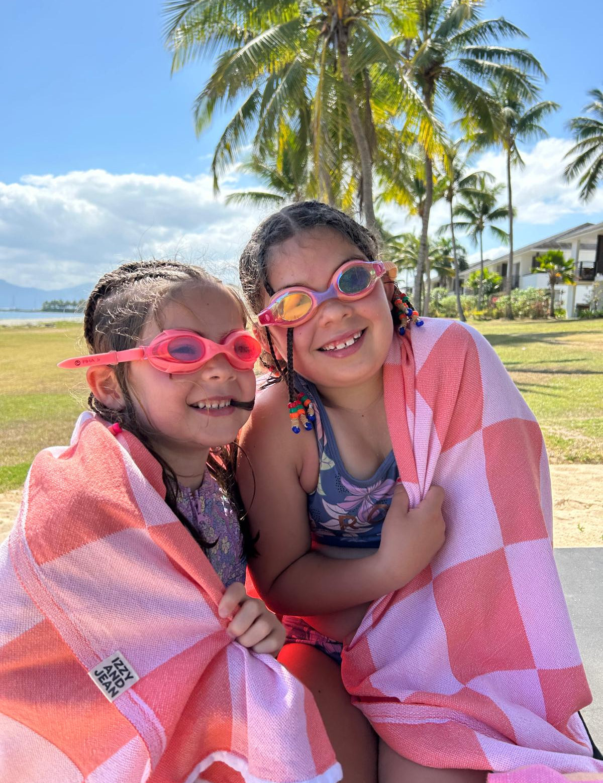 Two children wrapped in a pink towel on a beach with palm trees in the background