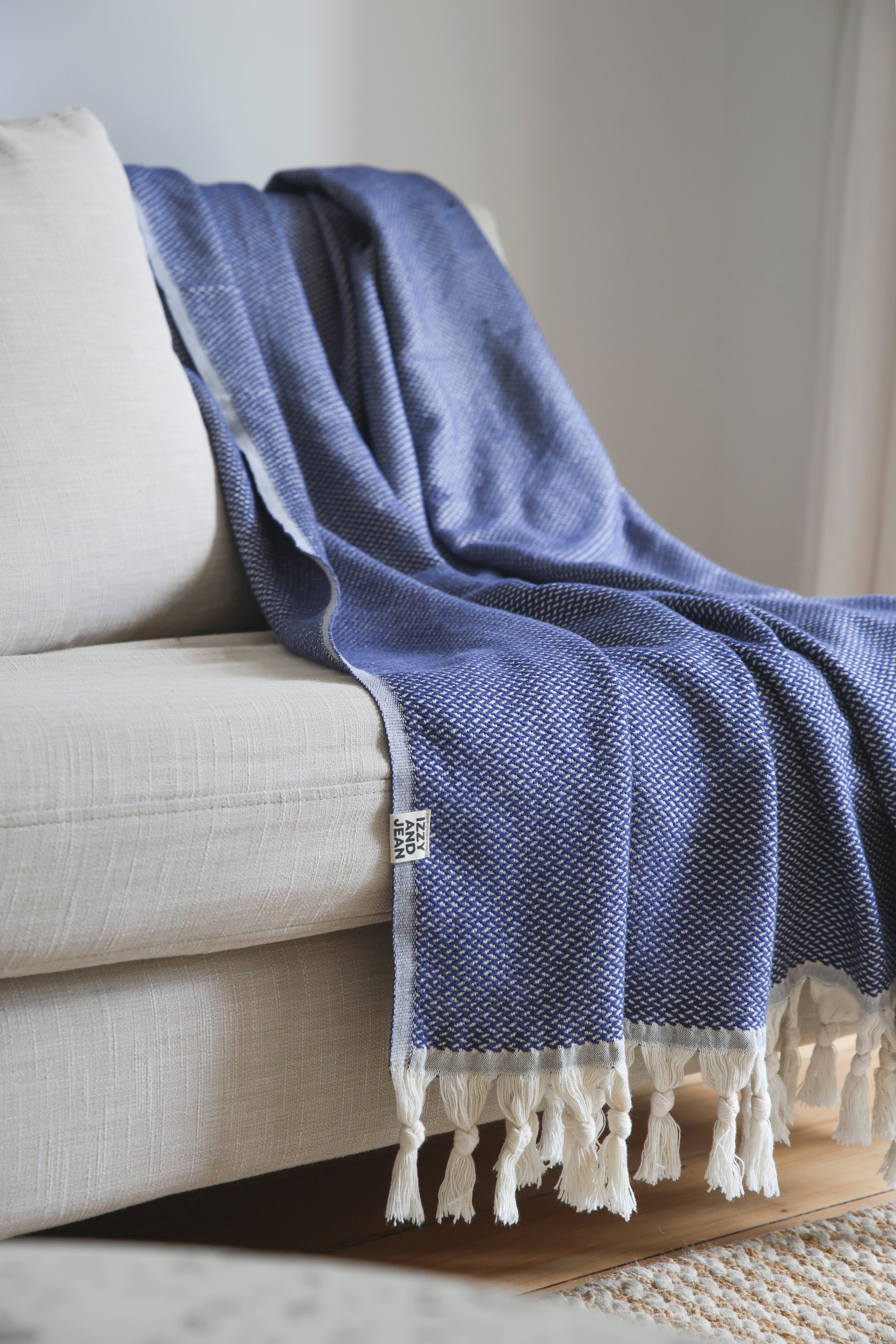 The Riveria Dark Blue throw blanket with tassels draped over a beige sofa.