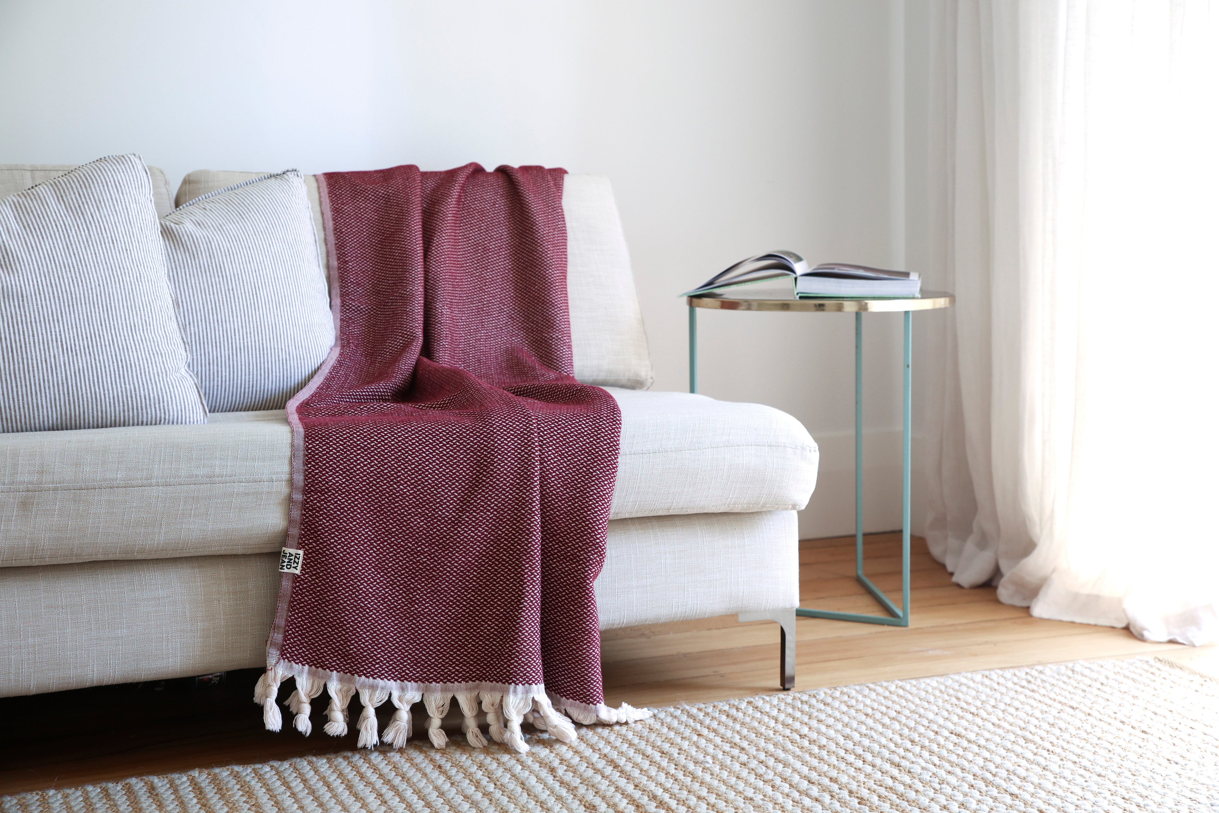 Burgandy throw blanket with white tassels strewn over the back and seat of a white sofa in a living room.