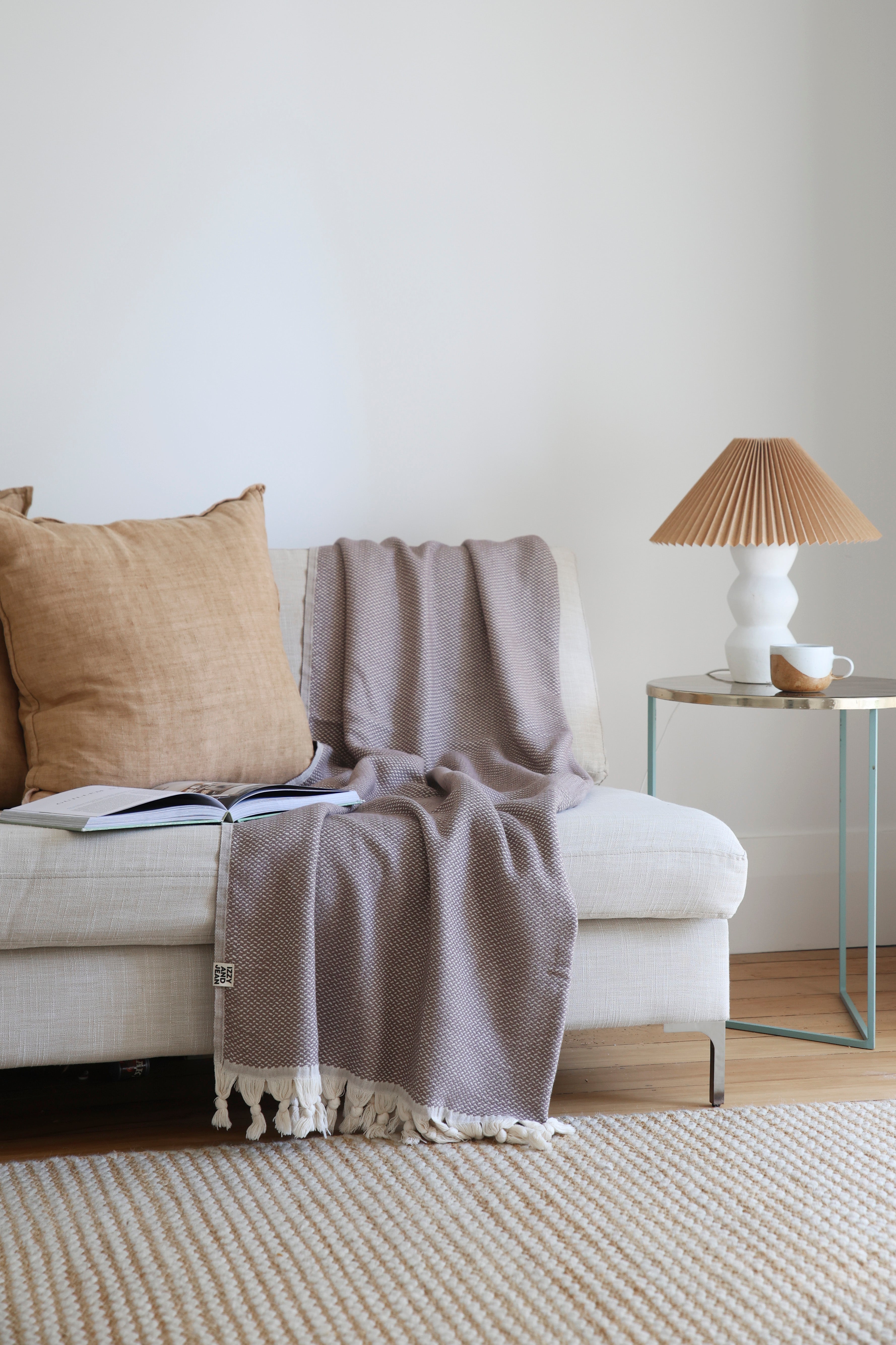 Brown throw blanket on a beige sofa with a lamp and coffee cup on a side table.