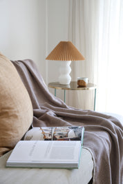 Cozy nook with a book, lamp, and the brown riveria throw blanket on the couch.