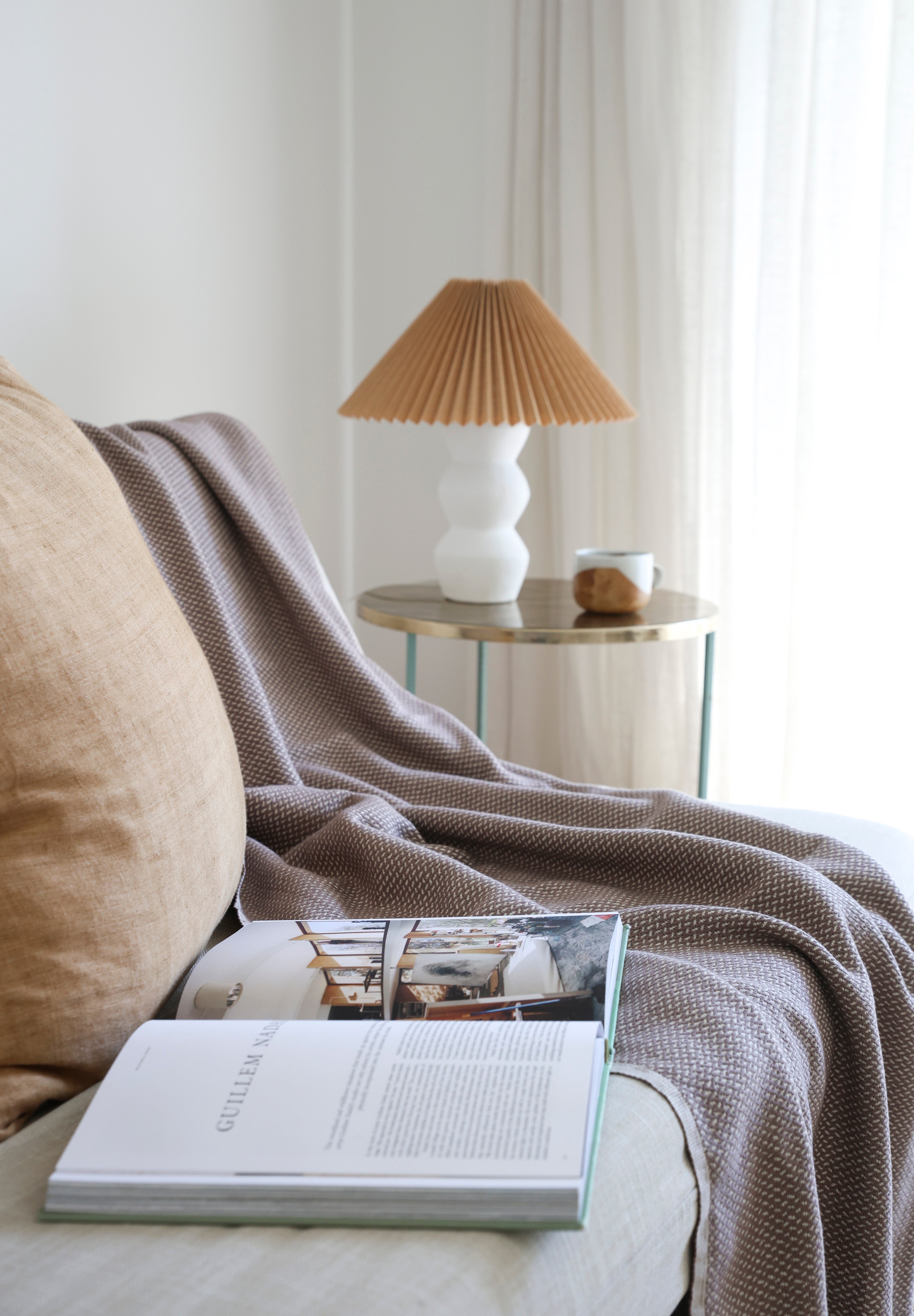 Cozy nook with a book, lamp, and the brown riveria throw blanket on the couch.