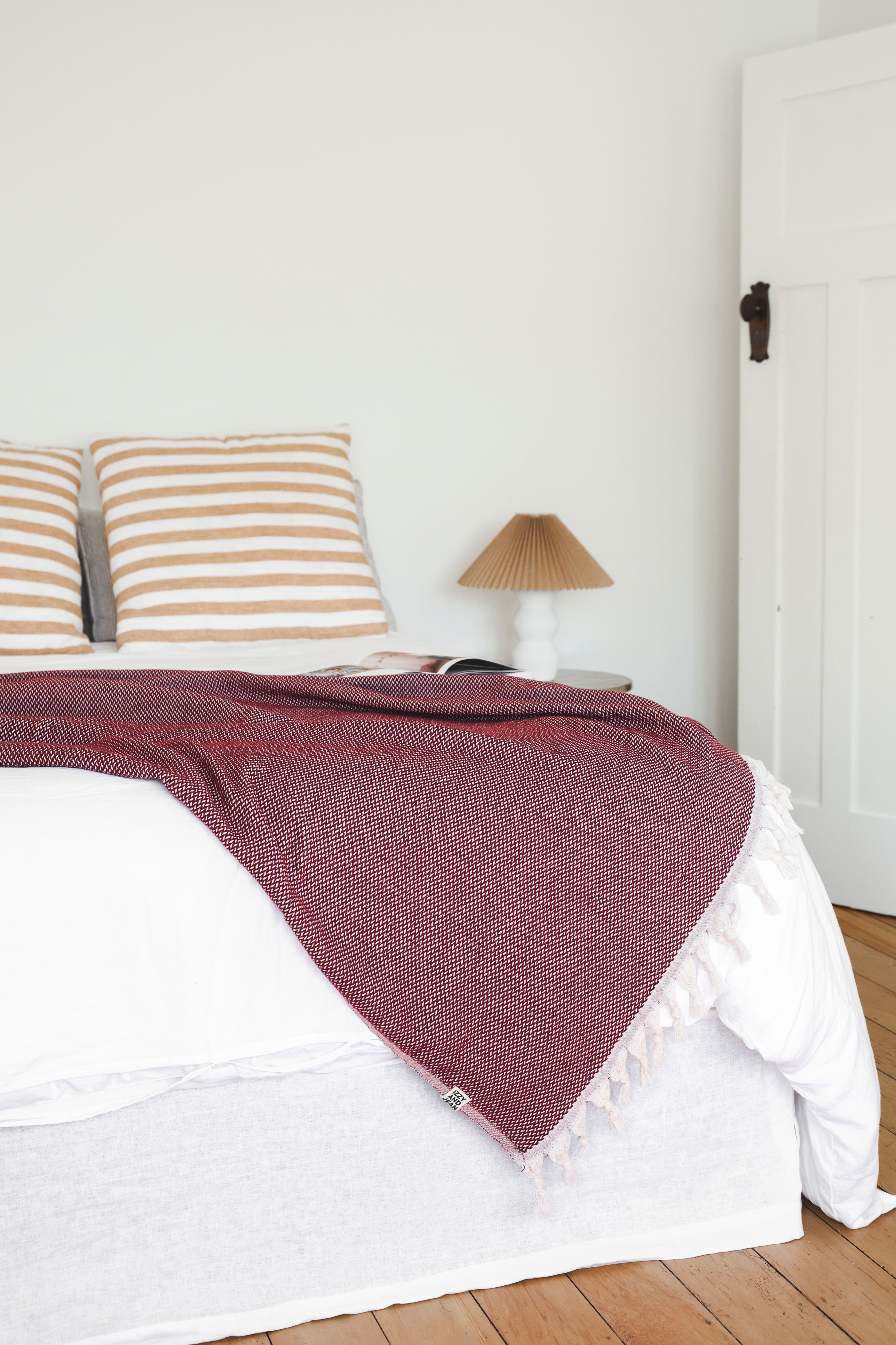 White bed spread and yellow striped pillows with a burgundy throw blanket in a simple room.