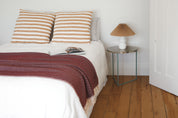 Bed with striped pillows and burgundy throw blanket next to a bedside table with a lamp.