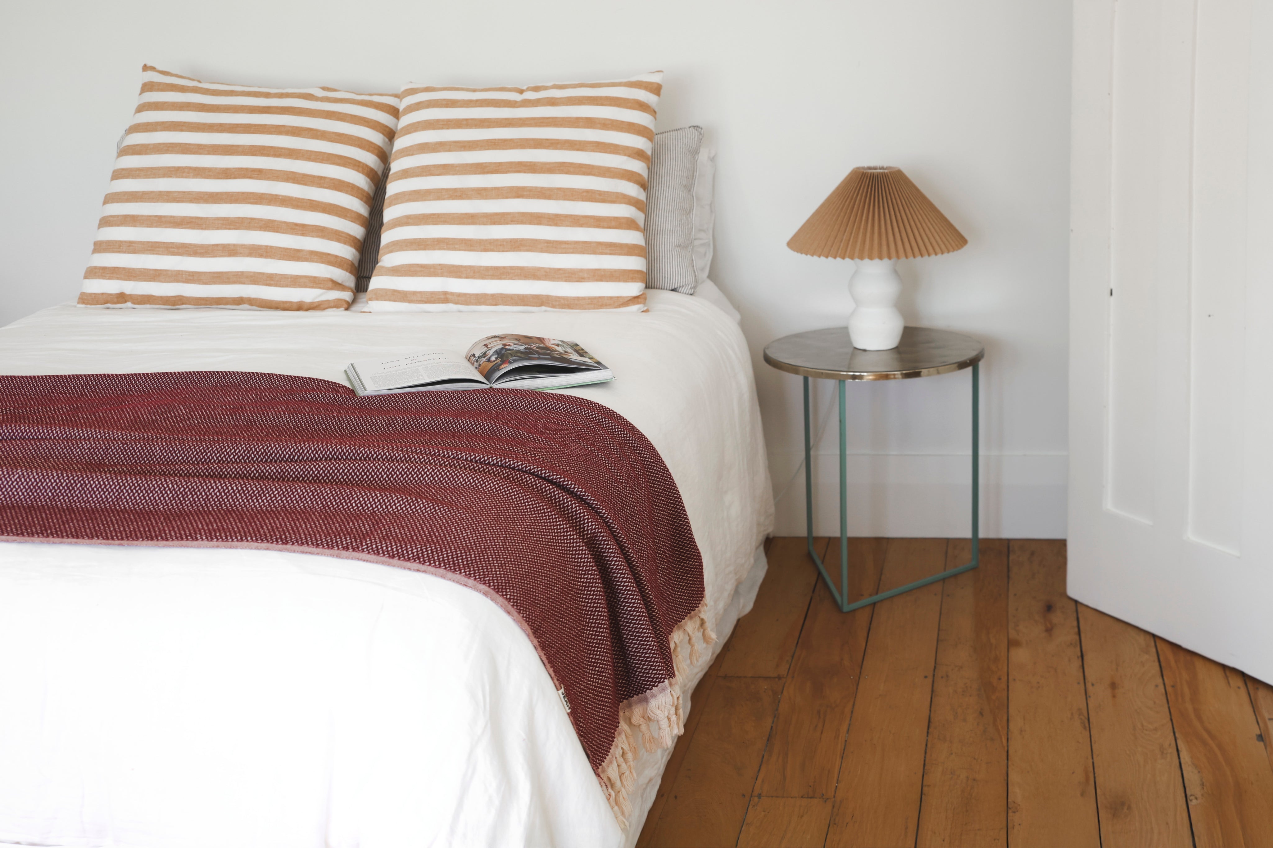 Bed with striped pillows and burgundy throw blanket next to a bedside table with a lamp.