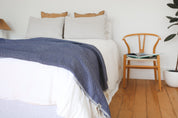 Bed with a dark blue riveria throw blanket and pillows in a bedroom setting.