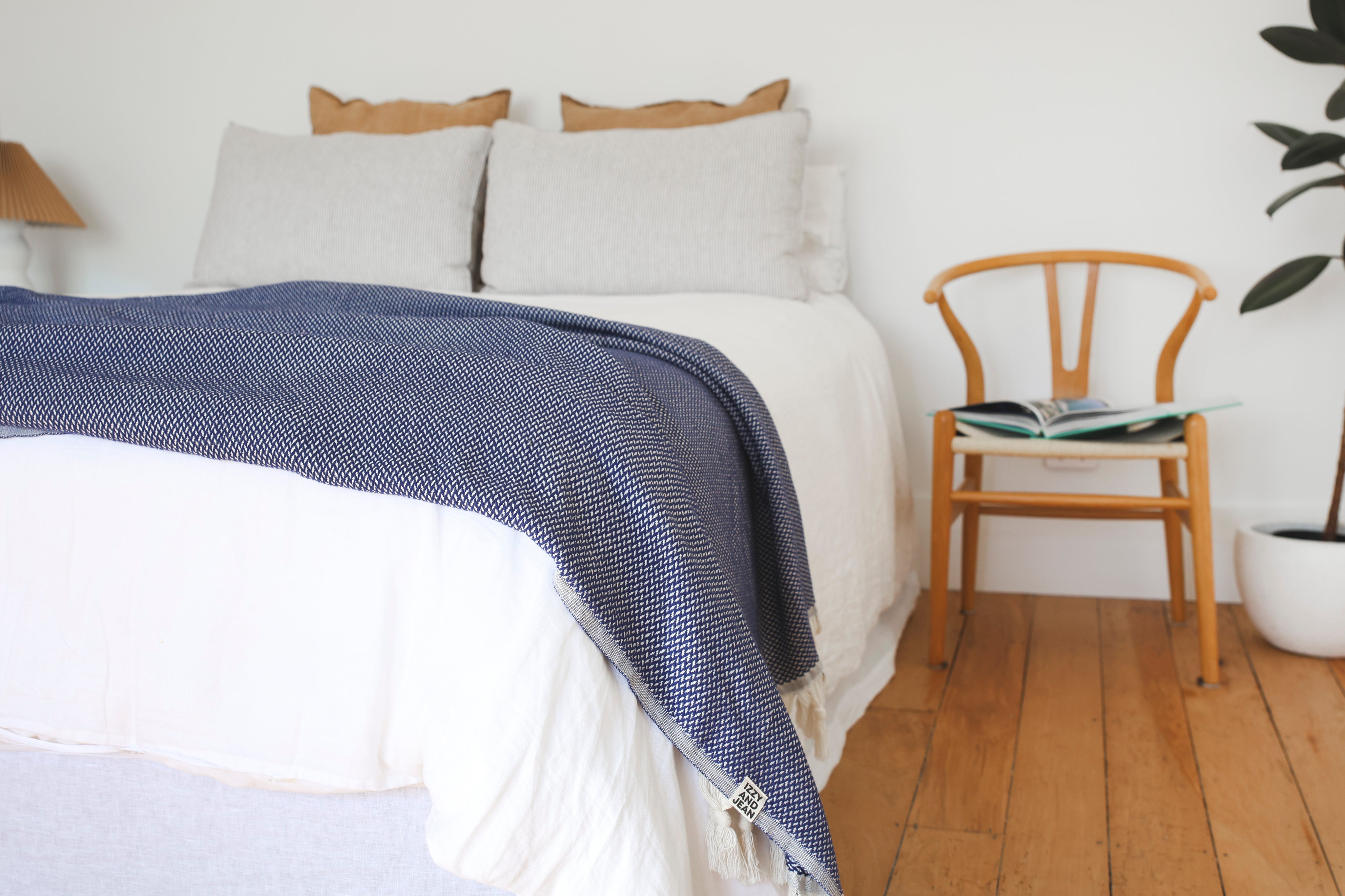Bed with a dark blue riveria throw blanket and pillows in a bedroom setting.