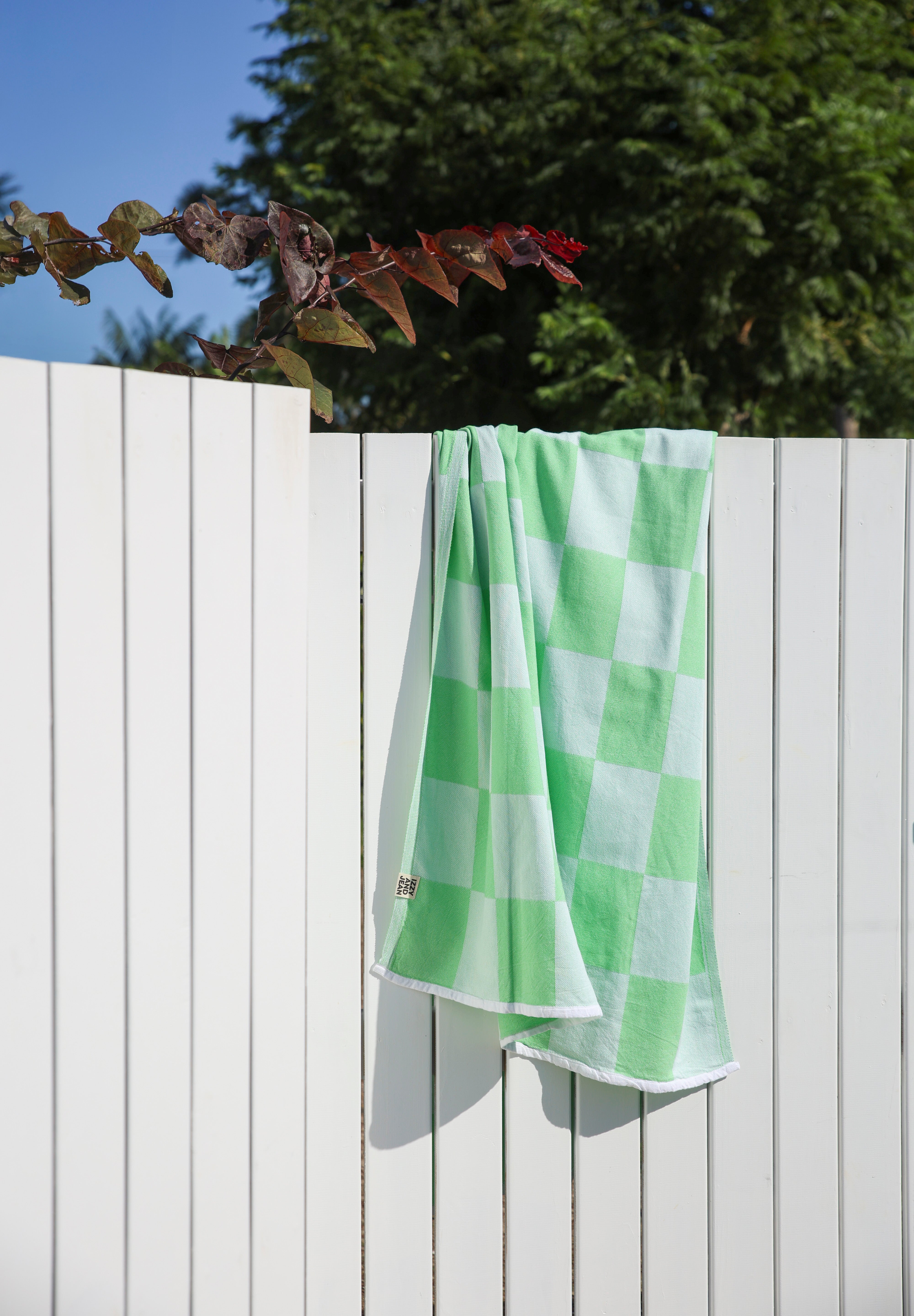 Green and white checkered towel hanging on a wooden fence with trees in the background
