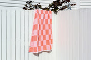 A Coral and white checkered Turkish towel hanging on a white wooden fence