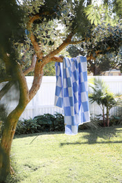 Blue and white checkered towel hanging on a tree branch in a garden setting