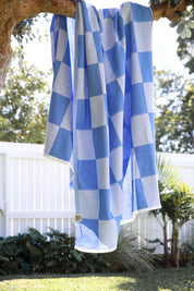Blue and white checkered towel hanging on a tree branch outdoors.