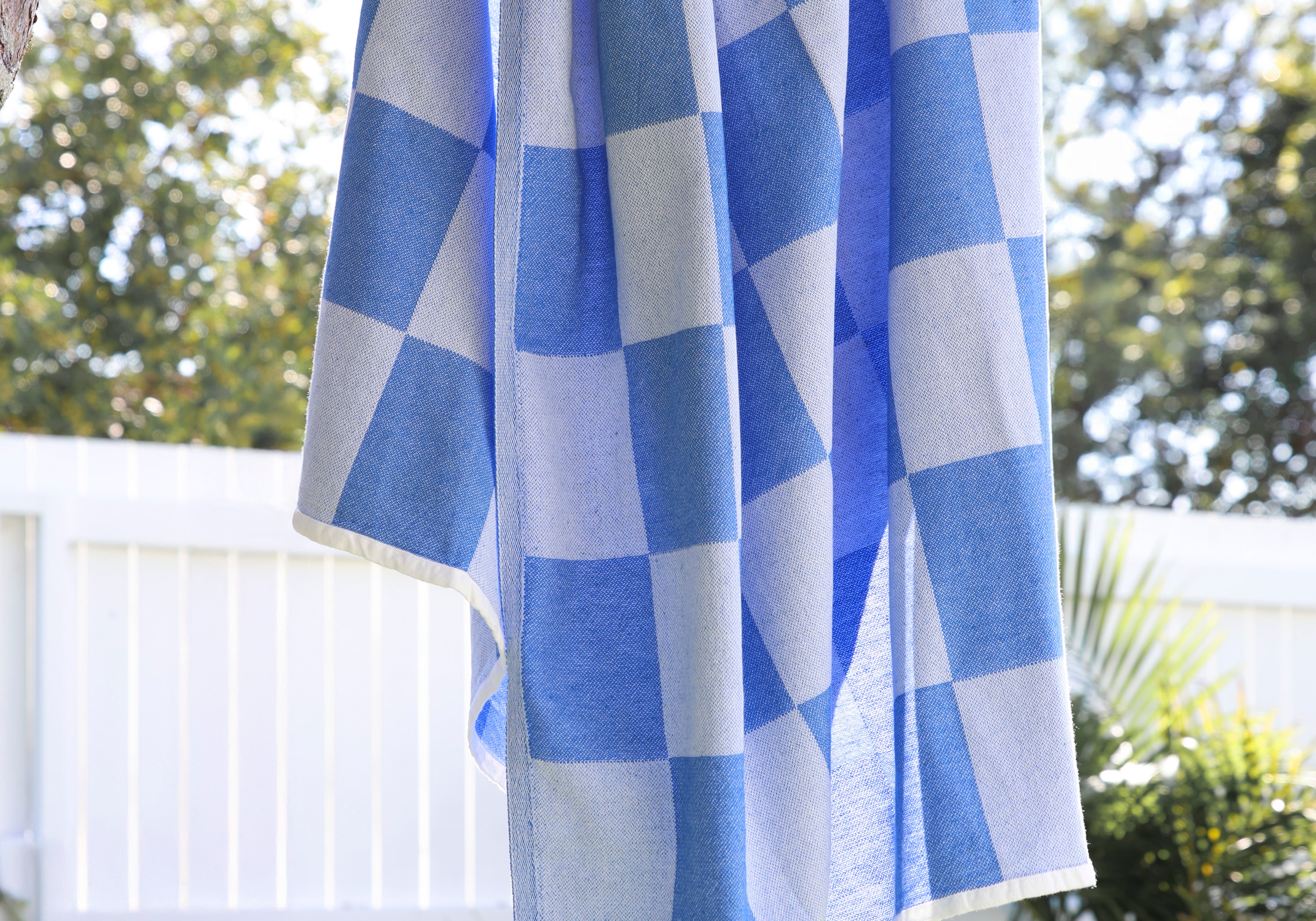 Blue and white checkered towel hanging on a tree branch outdoors.