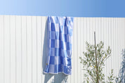 Blue and white checkered towel hanging on a white wooden fence with a clear blue sky.