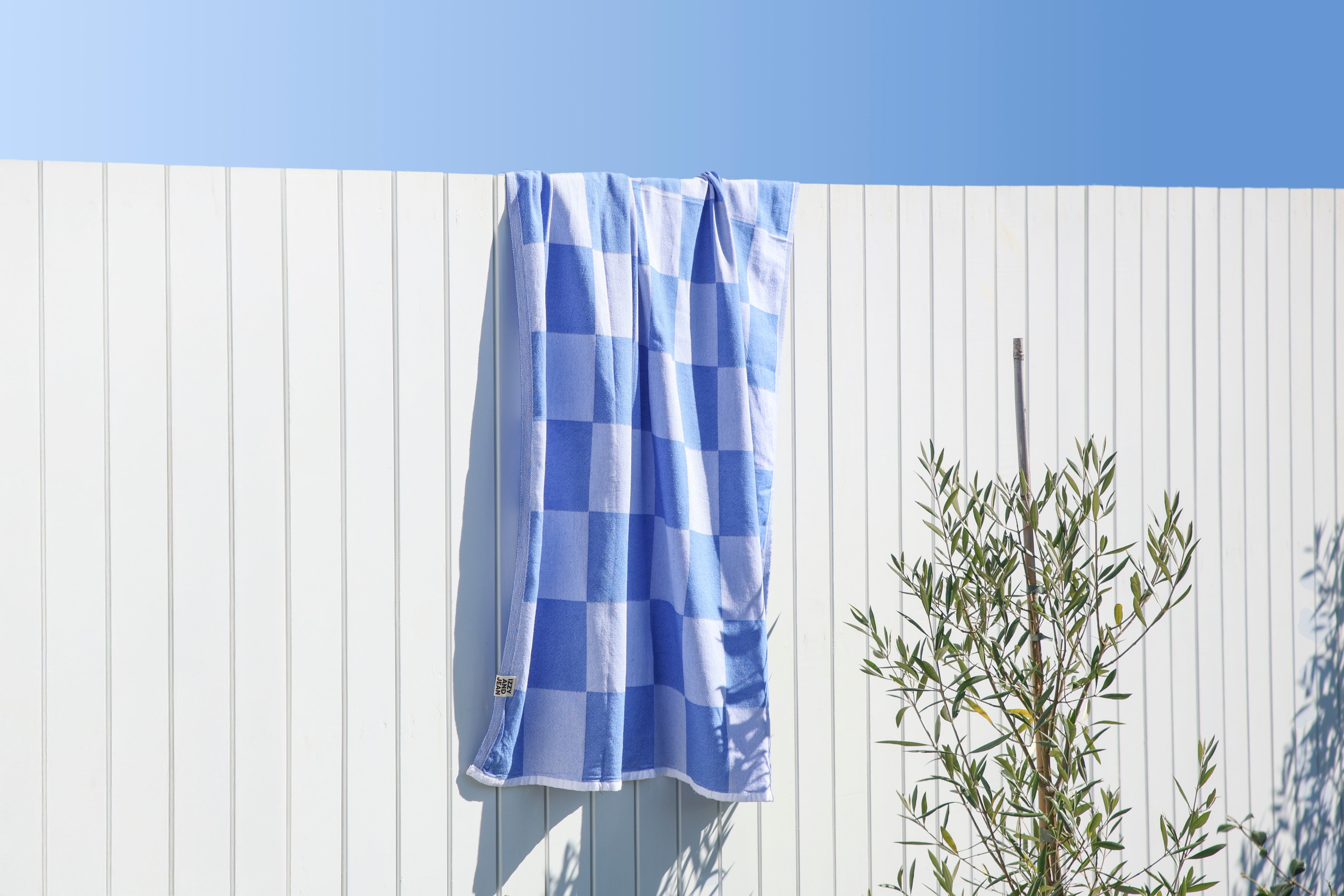 Blue and white checkered towel hanging on a white wooden fence with a clear blue sky.