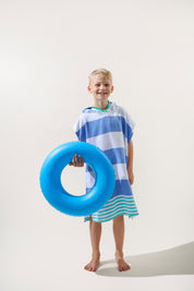 Child wearing a blue and green striped hooded ezy-towel holding a blue inflatable ring on a plain background