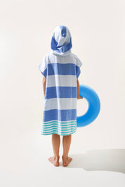 Child wearing a blue and green striped ezy-towel with a hood, made from cotton. Standing next to a blue inflatable ring on a white background.