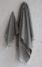 The Amalfi bathroom towel set. A white cotton soft quality bath sheet and hand towel with fluffy black dots and tassels, hanging on a wall.