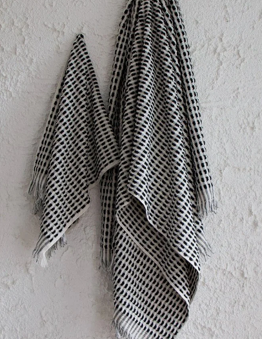 The Amalfi bathroom towel set. A white cotton soft quality bath sheet and hand towel with fluffy black dots and tassels, hanging on a wall.