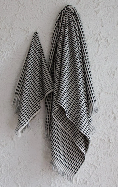 The Amalfi bathroom towel set. A white cotton soft quality bath sheet and hand towel with fluffy black dots and tassels, hanging on a wall.