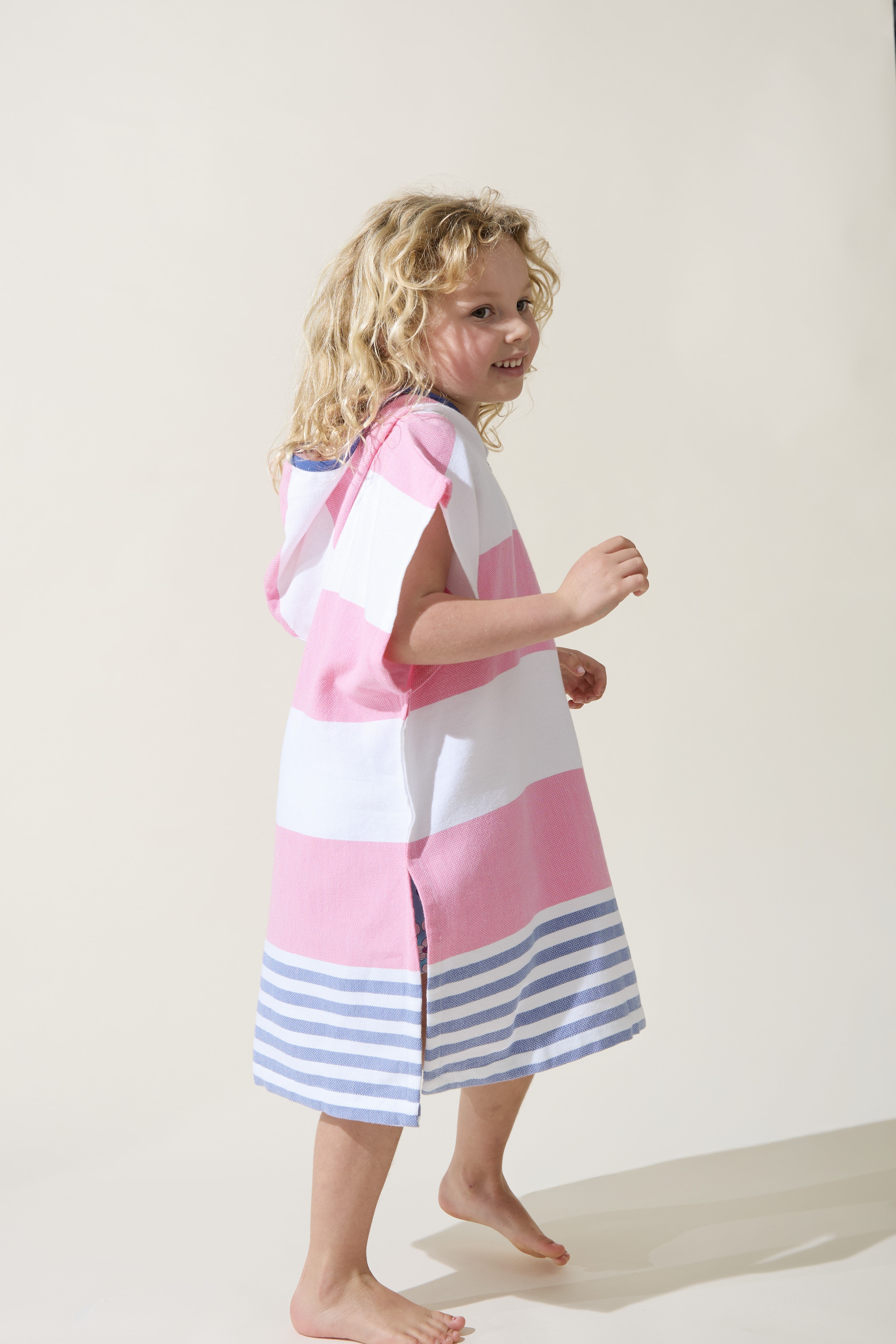 Child wearing a pink and white striped ezy-towel in pink and blue stripes, with a hood. On a plain background