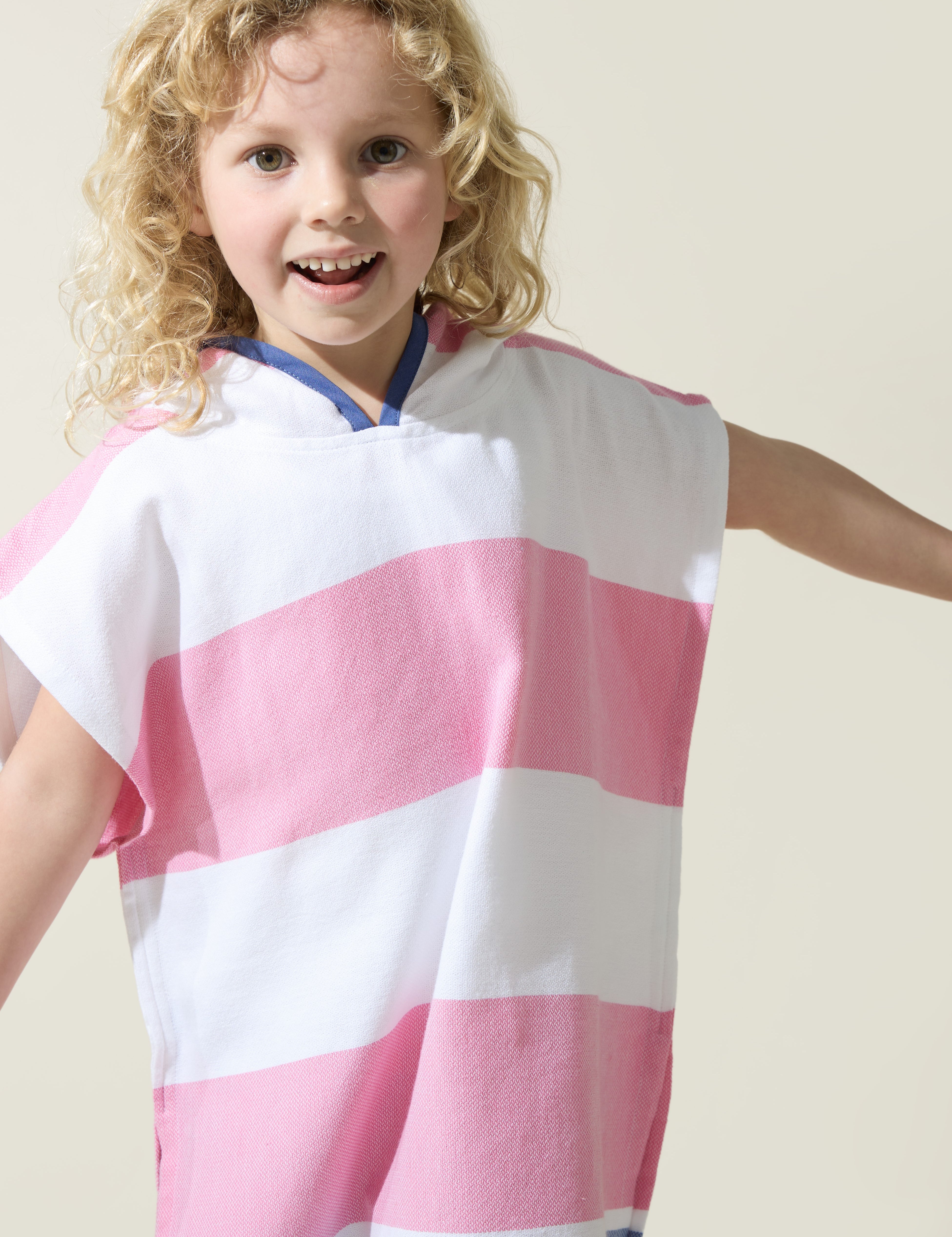Child wearing a pink and white striped hooded Turkish towel on a plain background