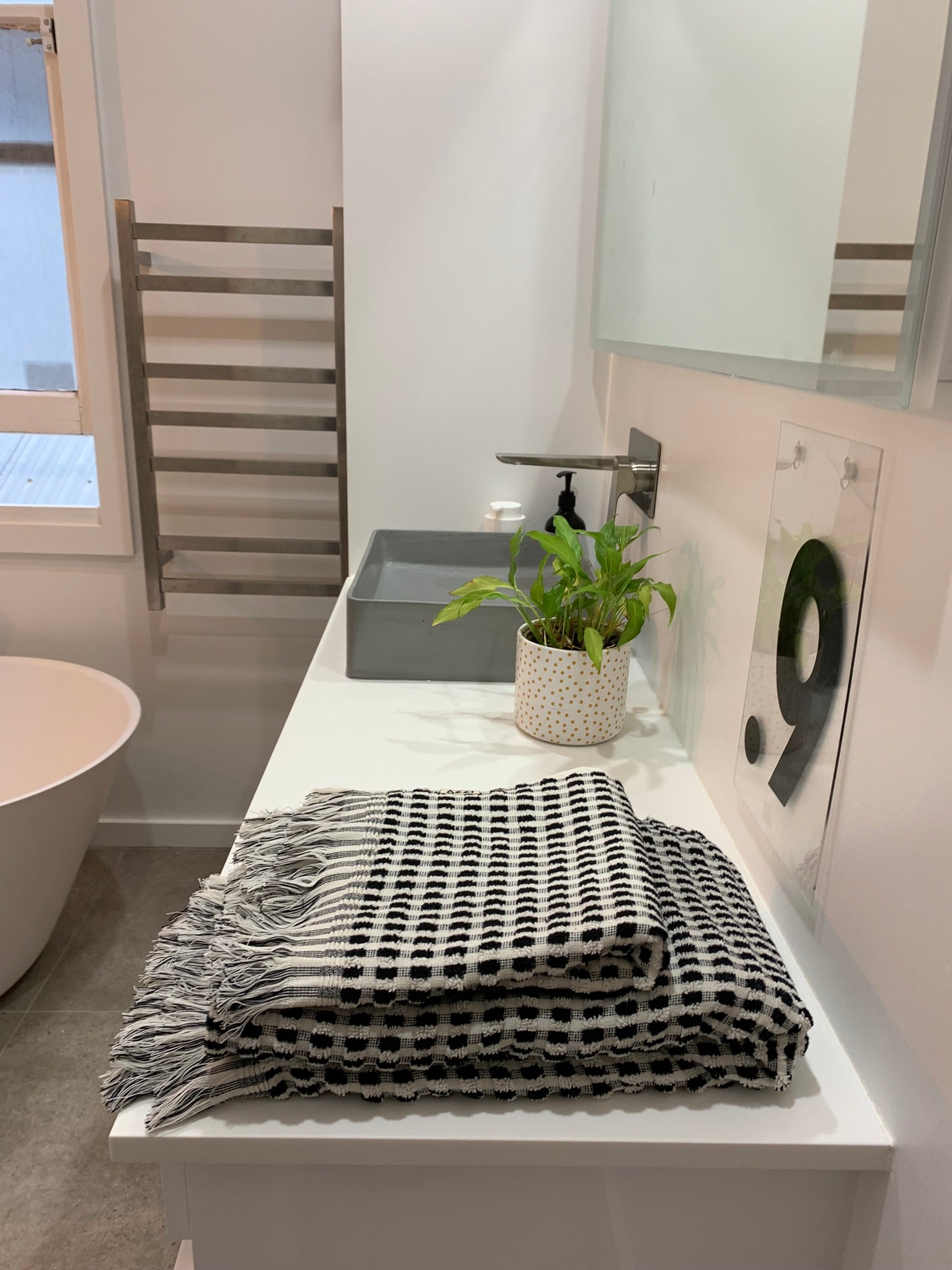 The Amalfi bathroom towel set with sheet and hand towel, in white with black dots in a checkered pattern and tassles.