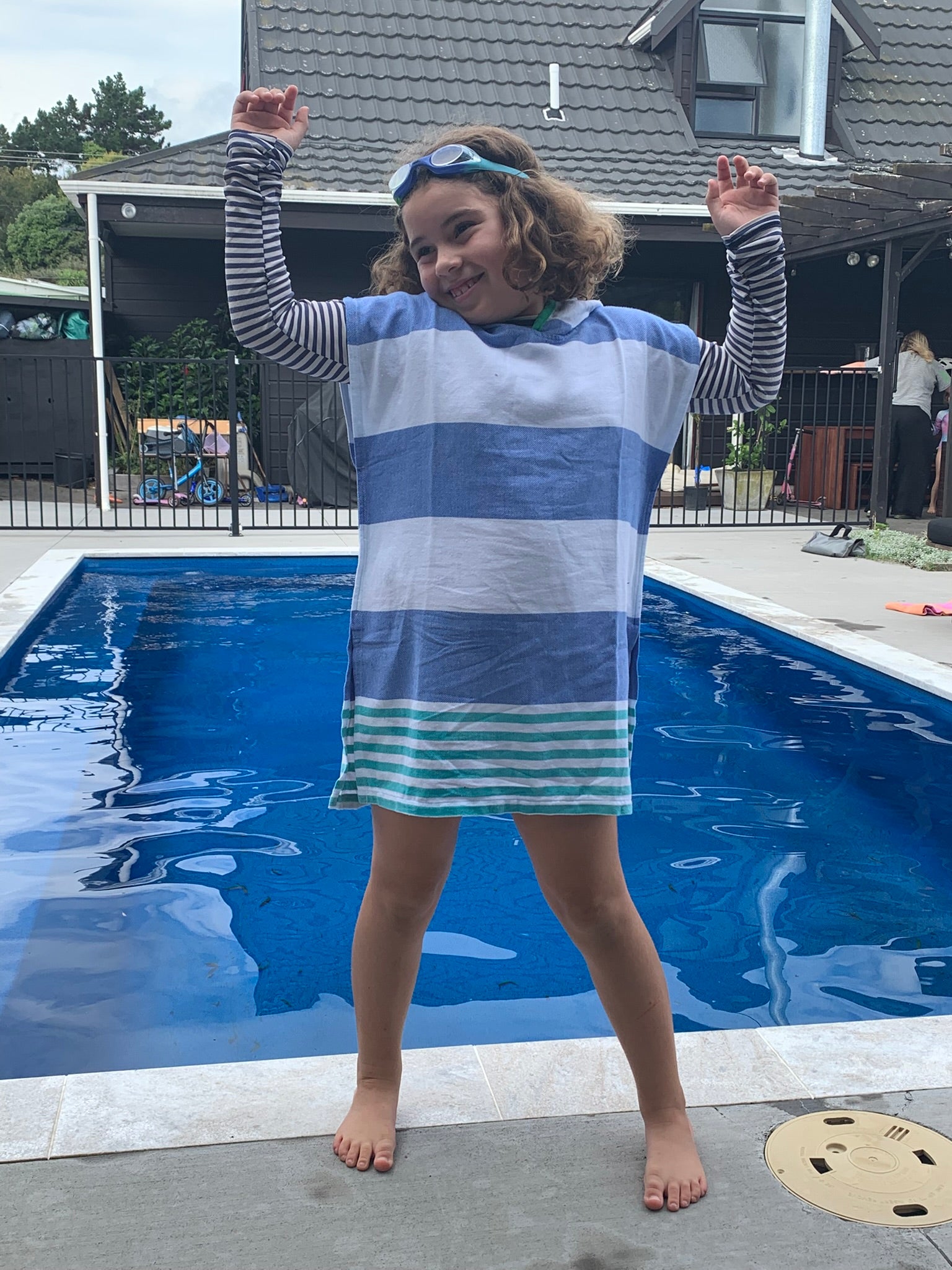 Child wearing a blue and green striped ezy-towel with hood by a pool