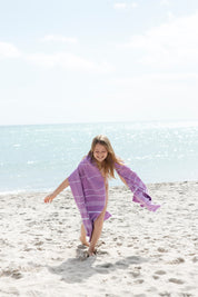 A little girl playing in the sand with the classic purple turkish towel over her shoulders and the sea in the background