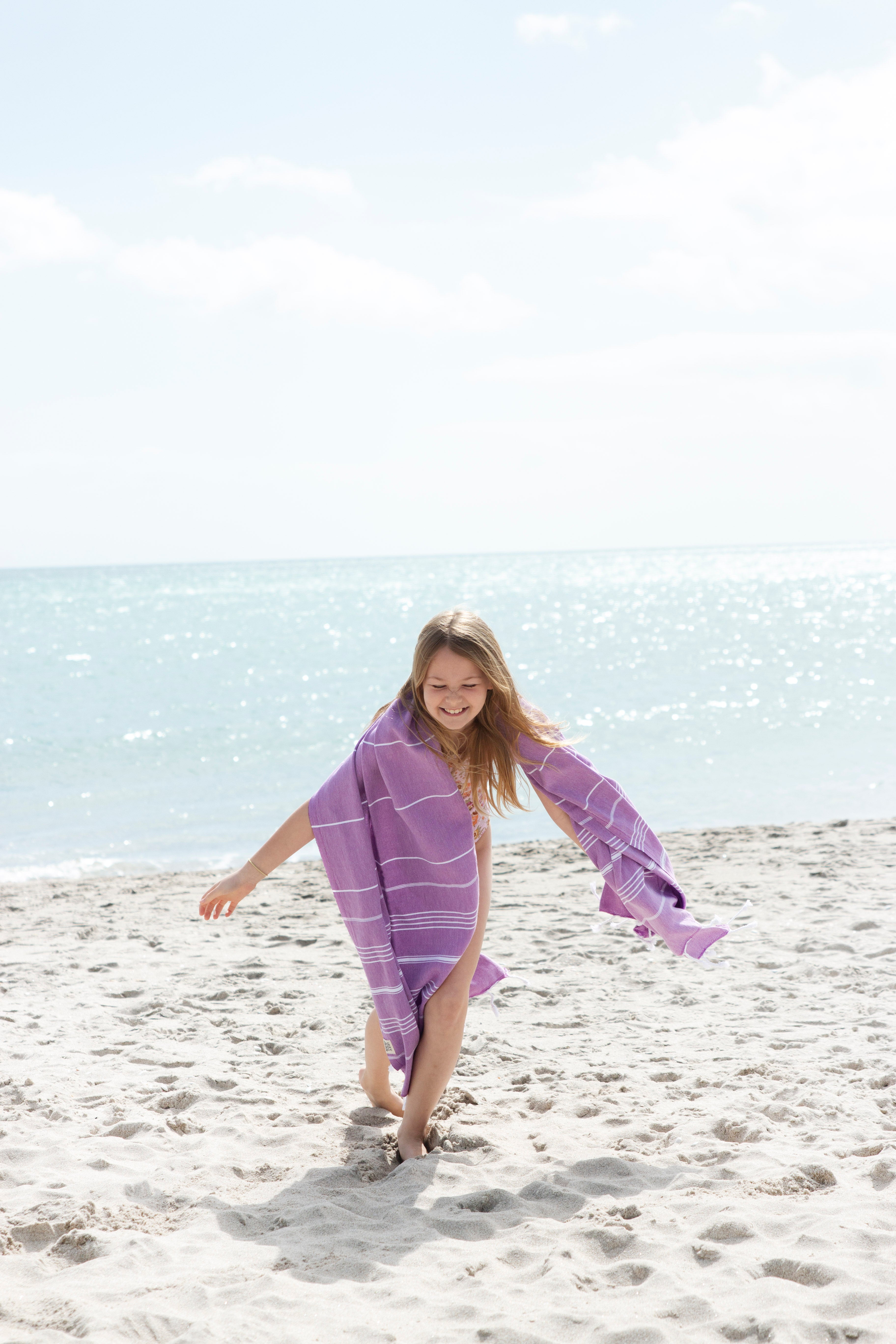A little girl playing in the sand with the classic purple turkish towel over her shoulders and the sea in the background