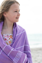 A little girl wearing a purple classic Turkish towel over her  bathing suit on the beach