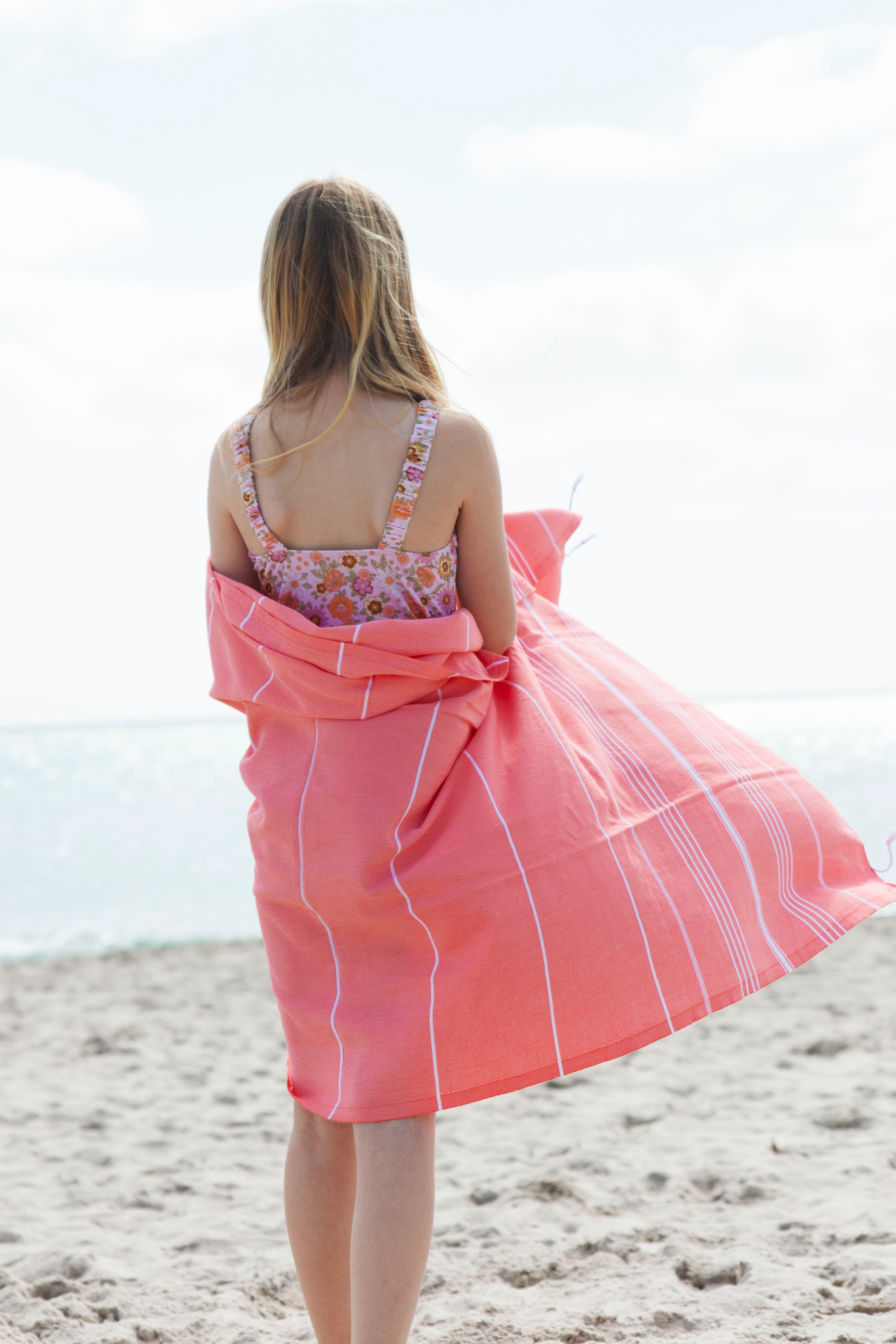  A girl on a beach wrapped in a coral Classic Turkish Towel