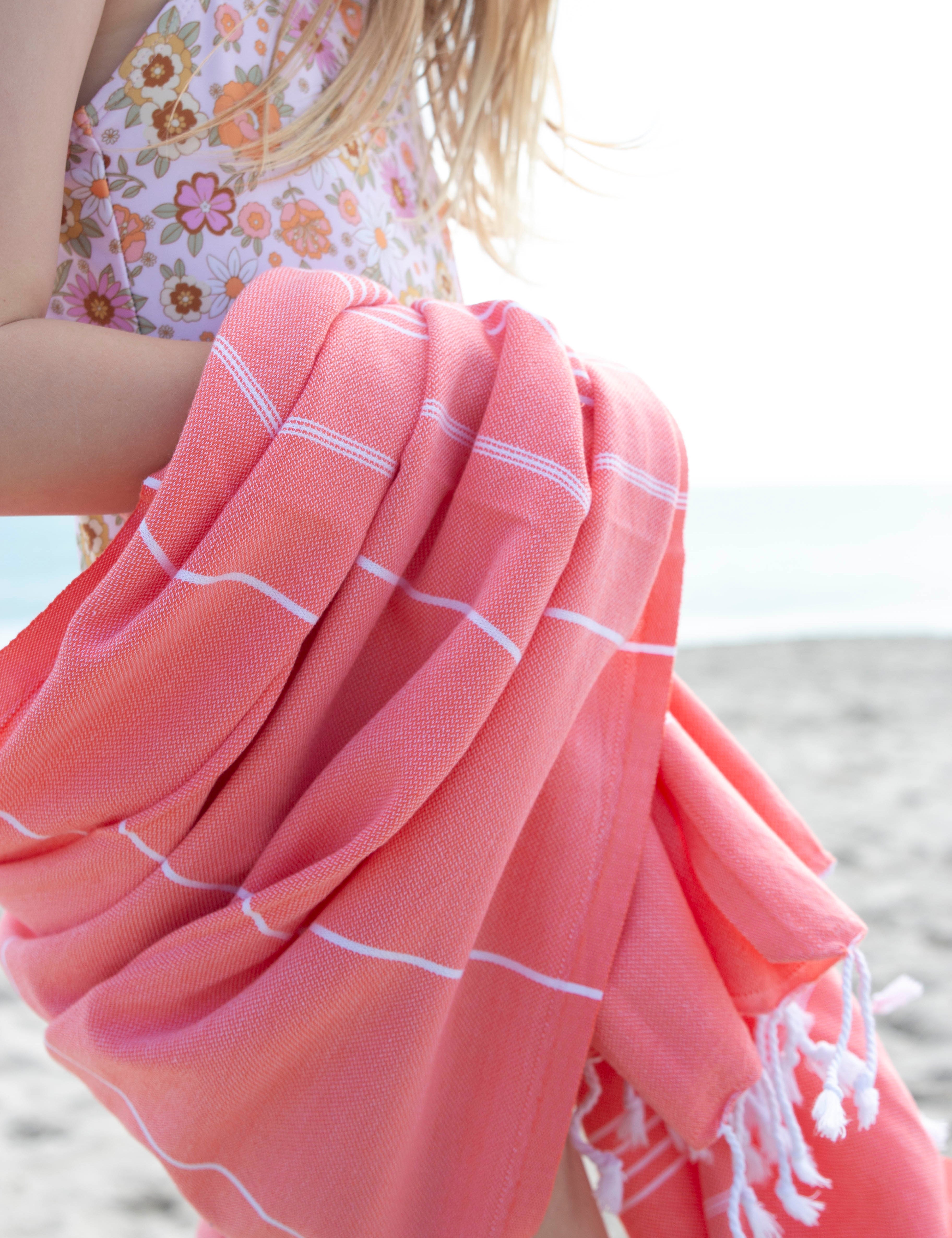 A close up of the Classic Coral Turkish towel wrapped around a girl wearing a floral bathing suit on the beach
