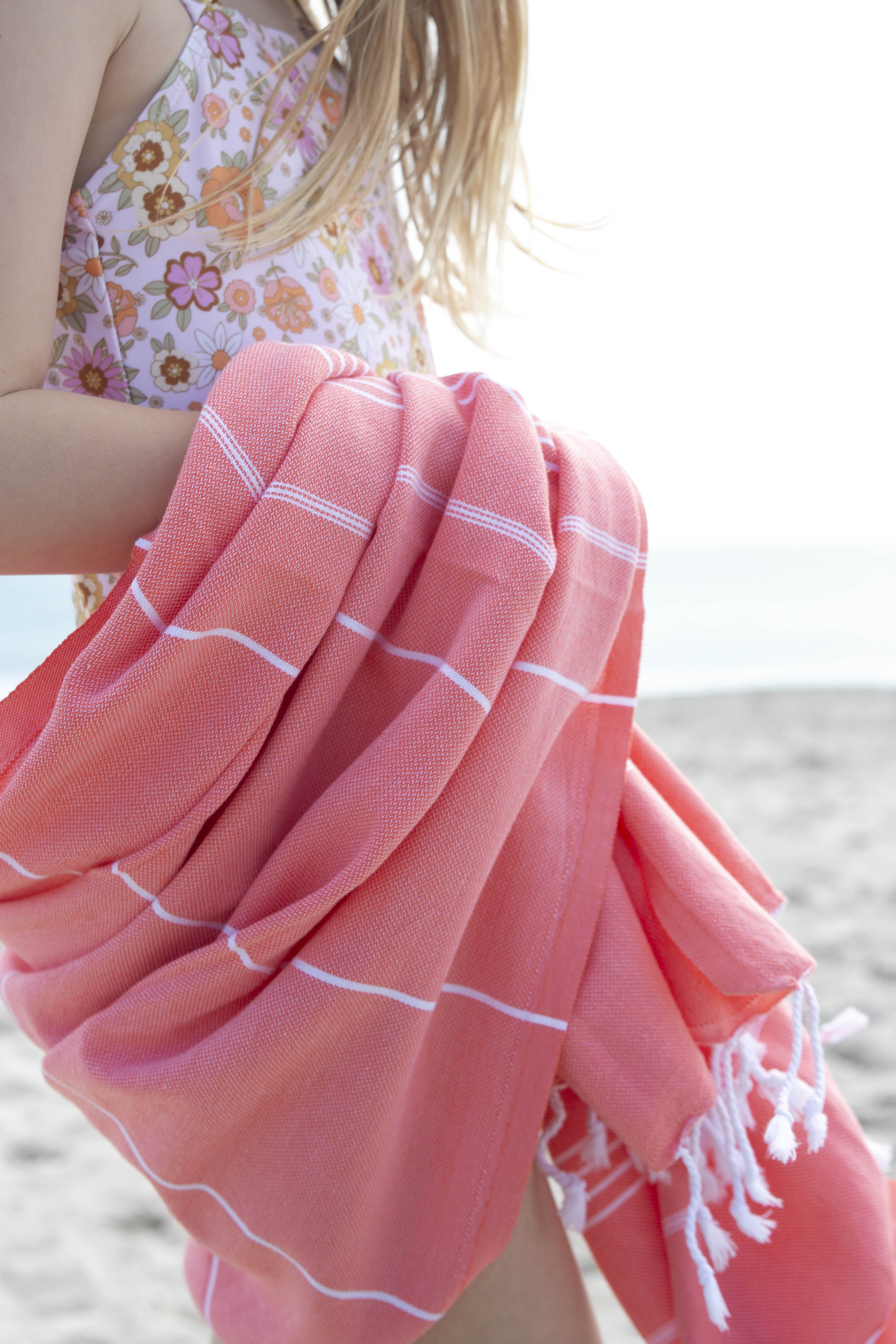 A close up of the Classic Coral Turkish towel wrapped around a girl wearing a floral bathing suit on the beach
