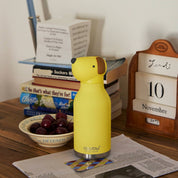 Yellow dog-shaped bottle on a wooden surface with books and a calendar in the background