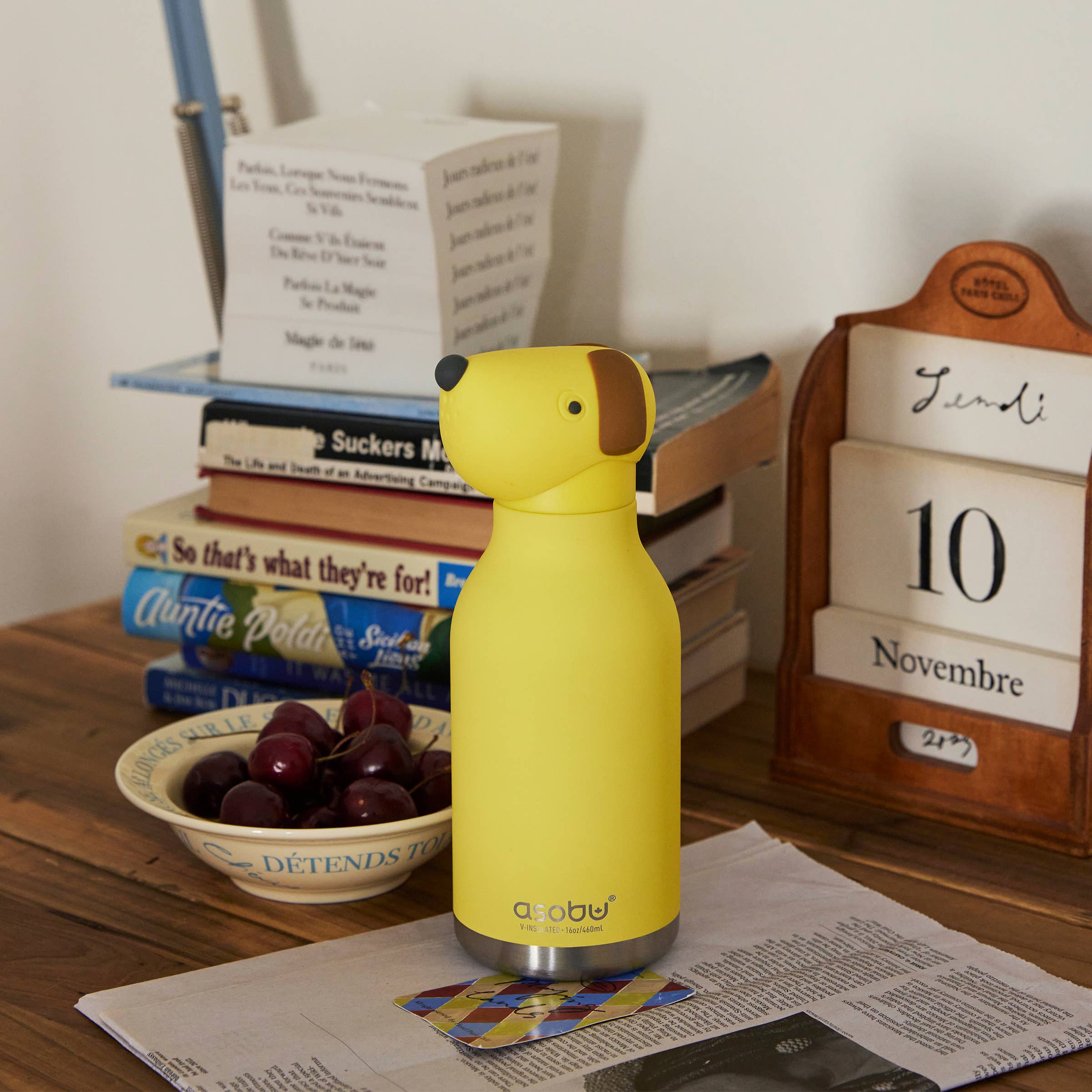 Yellow dog-shaped bottle on a wooden surface with books and a calendar in the background