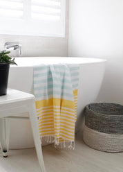 a mint, yellow and white striped Turkish towel hanging in the side of a bath