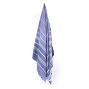A navy Turkish towel with white stripes and fringes on the bottom hangs on a hook