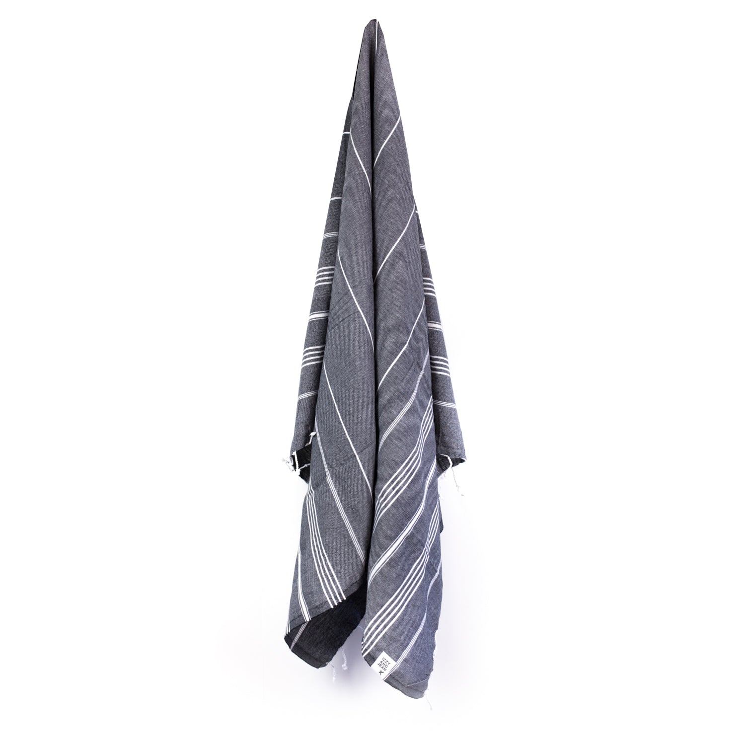 A black Turkish towel with white stripes and fringes on the bottom hanging on a hook with a white background.