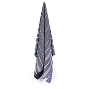 A black Turkish towel with white stripes and fringes on the bottom hanging on a hook with a white background.