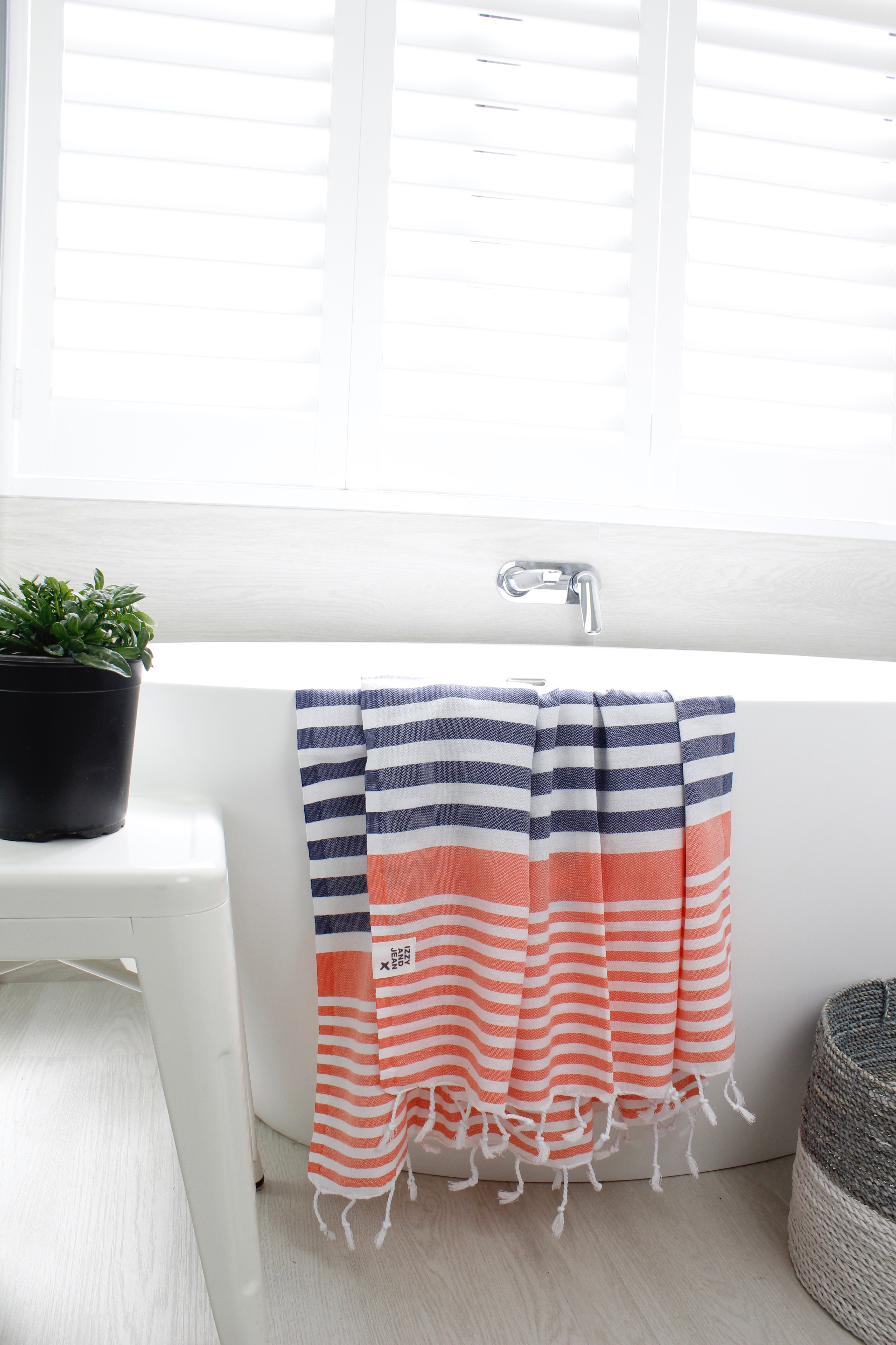 A blue and coral stripped Turkish towel hanging over the side of a stylish white bath.