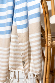 A close up of a draped Sofia Turkish towel with sky blue, white and sand stripes, and white fringes at the bottom