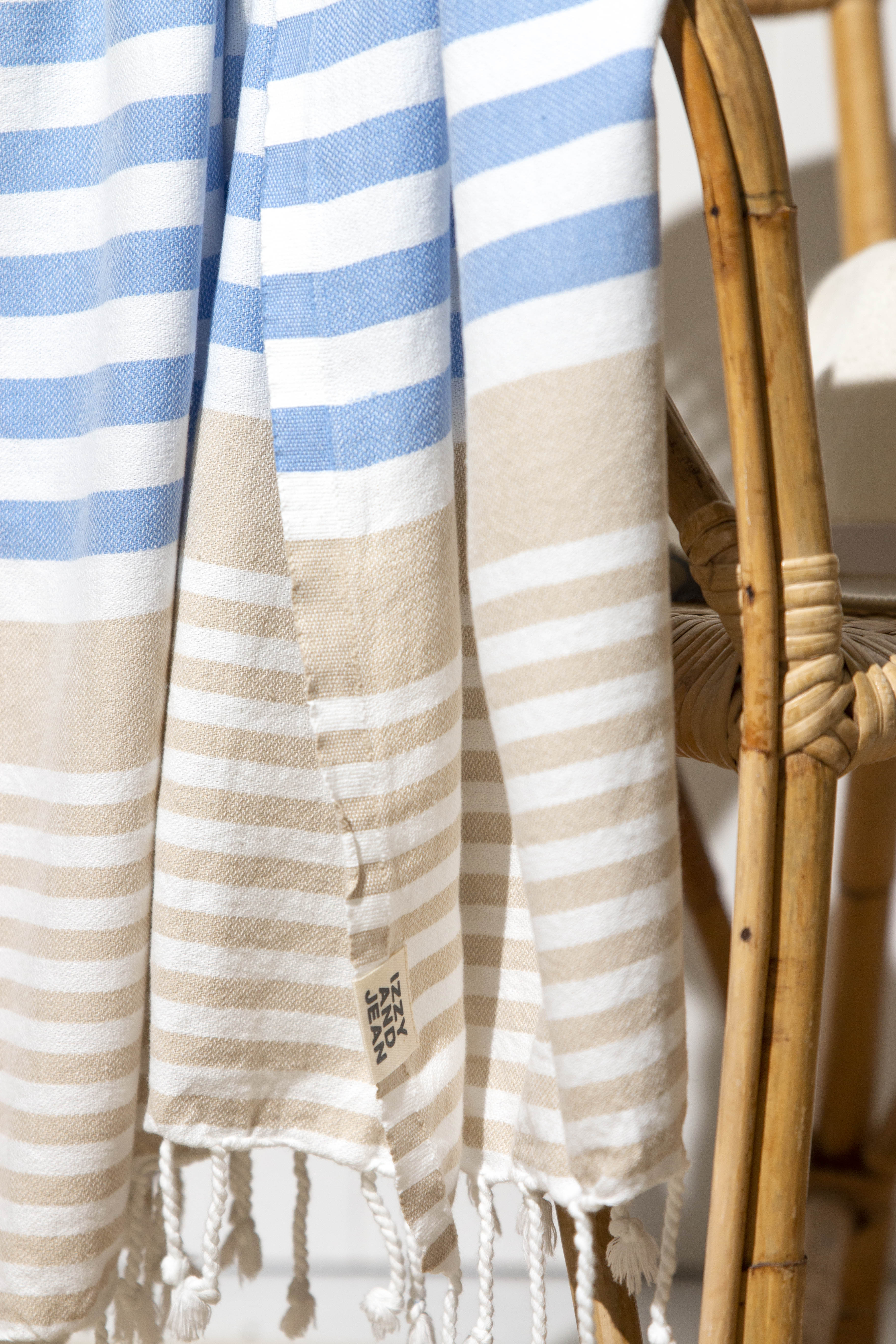 A close up of a draped Sofia Turkish towel with sky blue, white and sand stripes, and white fringes at the bottom