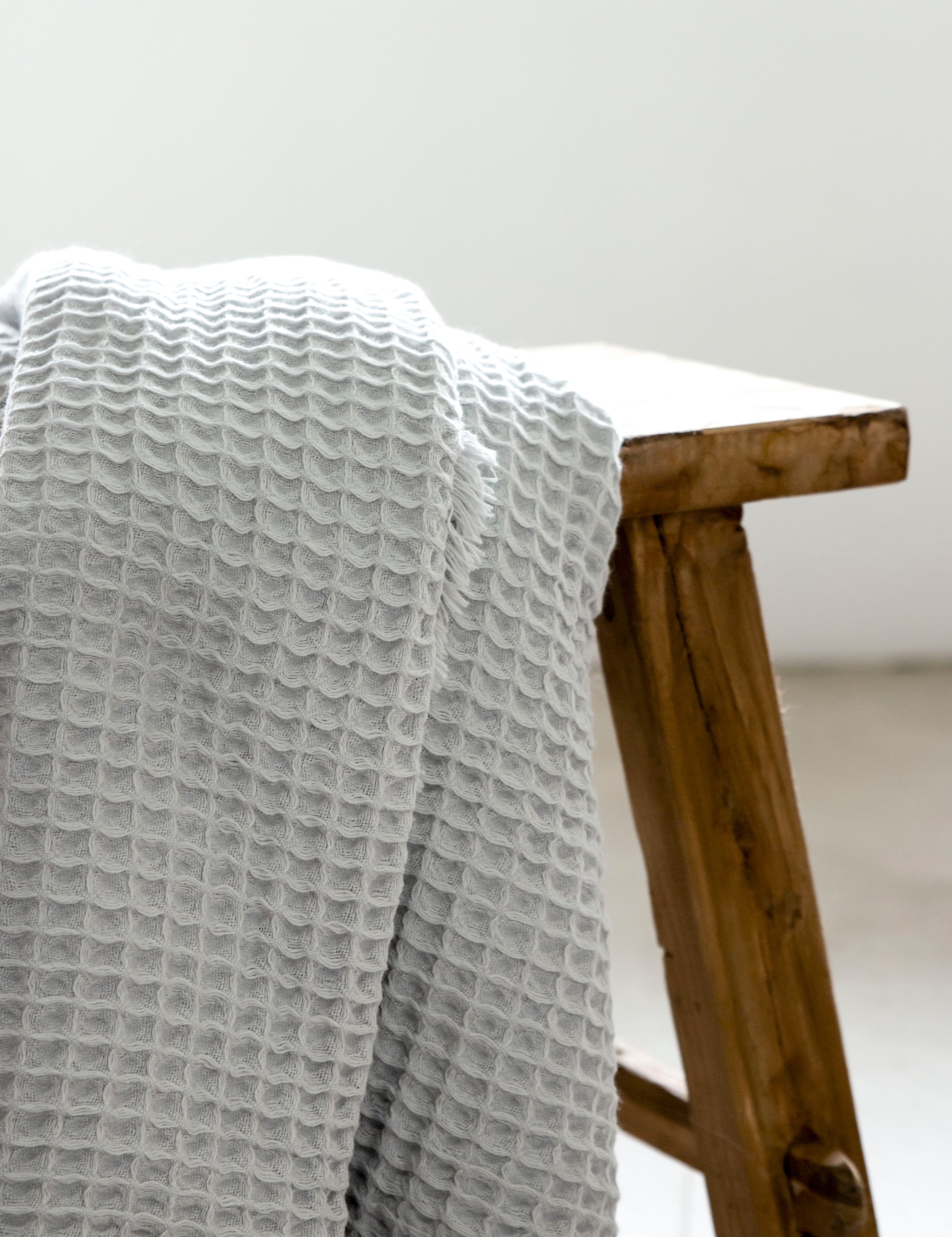 A pale grey waffle bath towel hanging on a wooden stool.
