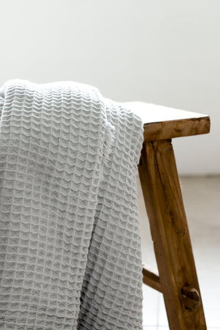 A pale grey coloured waffle bath towel folded on a white background