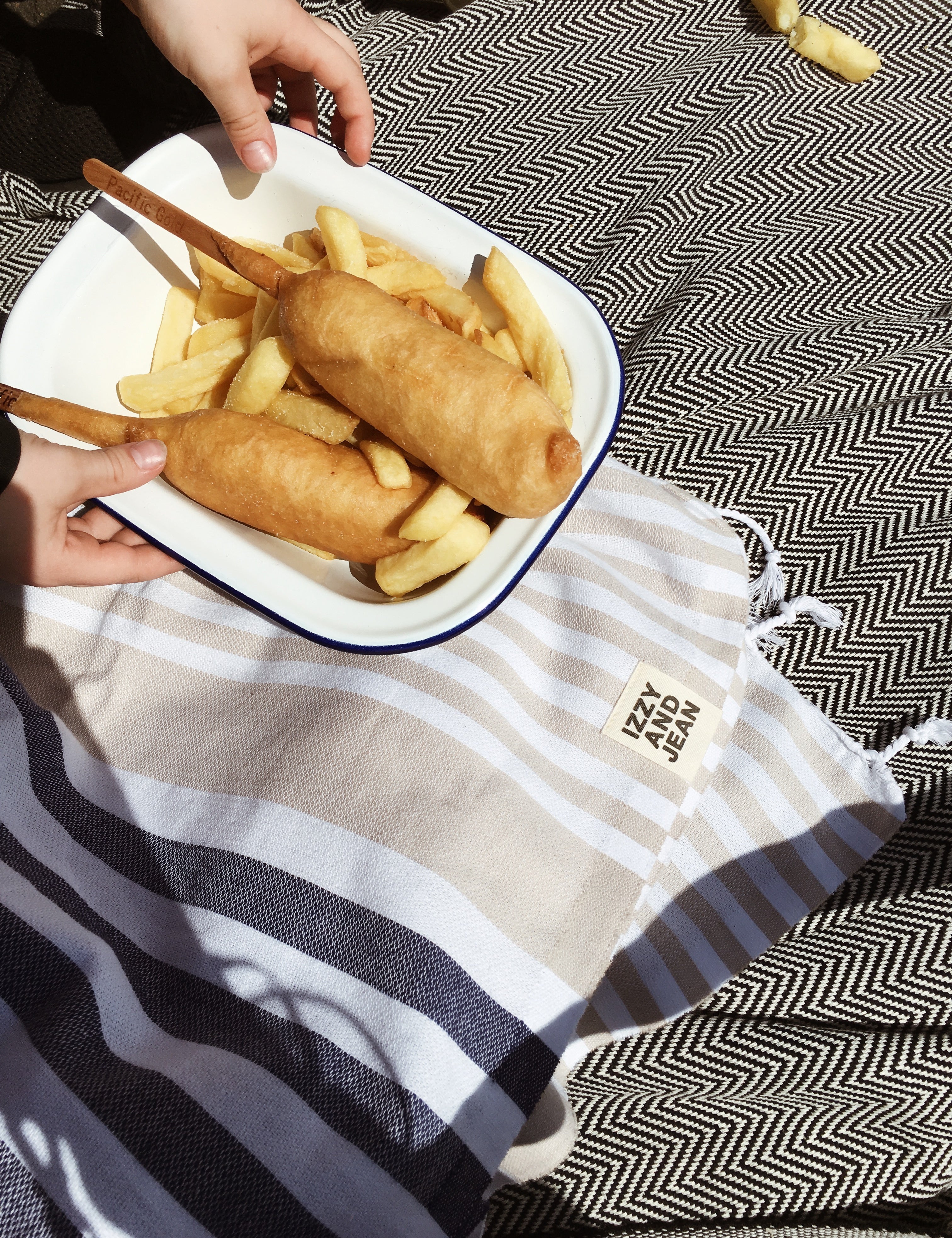 Fish and Chipes on a plate sitting on a  Navy and Sand striped Sofia Turkish Towel with tassles at the bottom