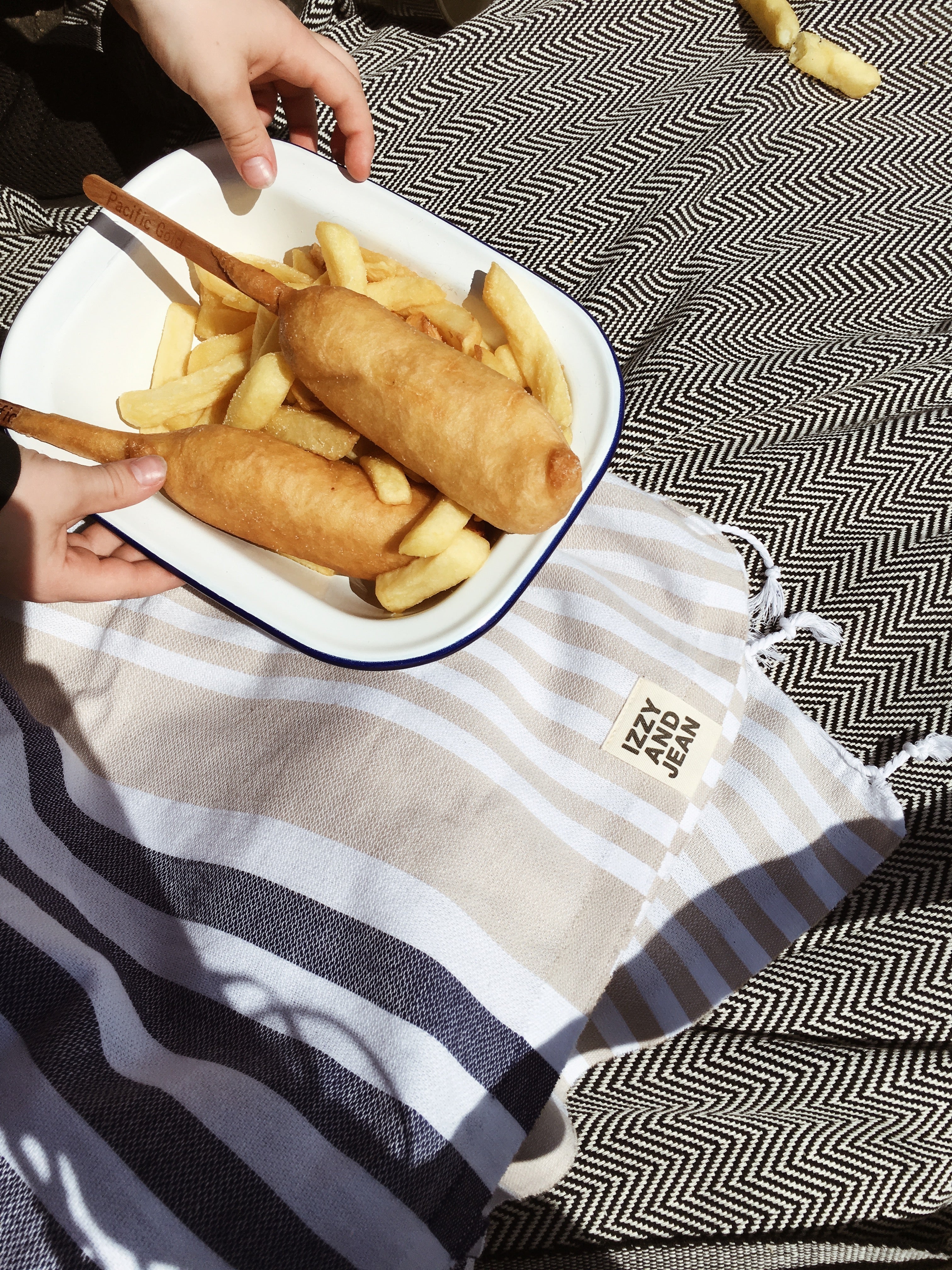Fish and Chipes on a plate sitting on a  Navy and Sand striped Sofia Turkish Towel with tassles at the bottom