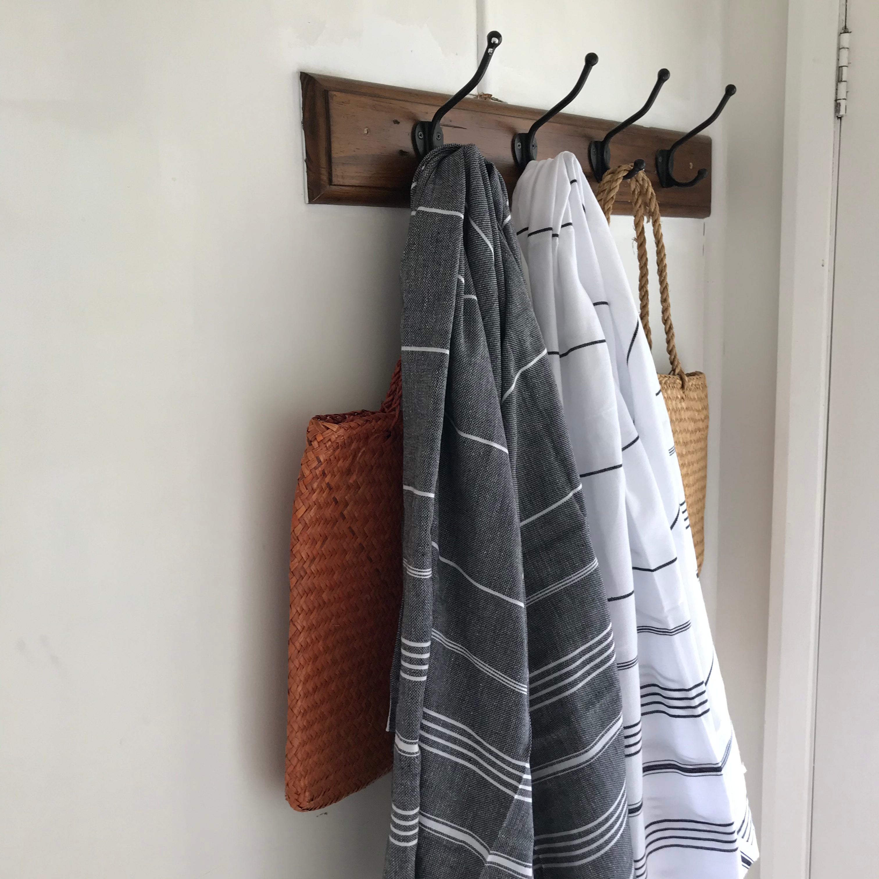 Turkish towels in black and white hanging side by side on hooks, with white and black striped respectively, and fringes on the bottom
