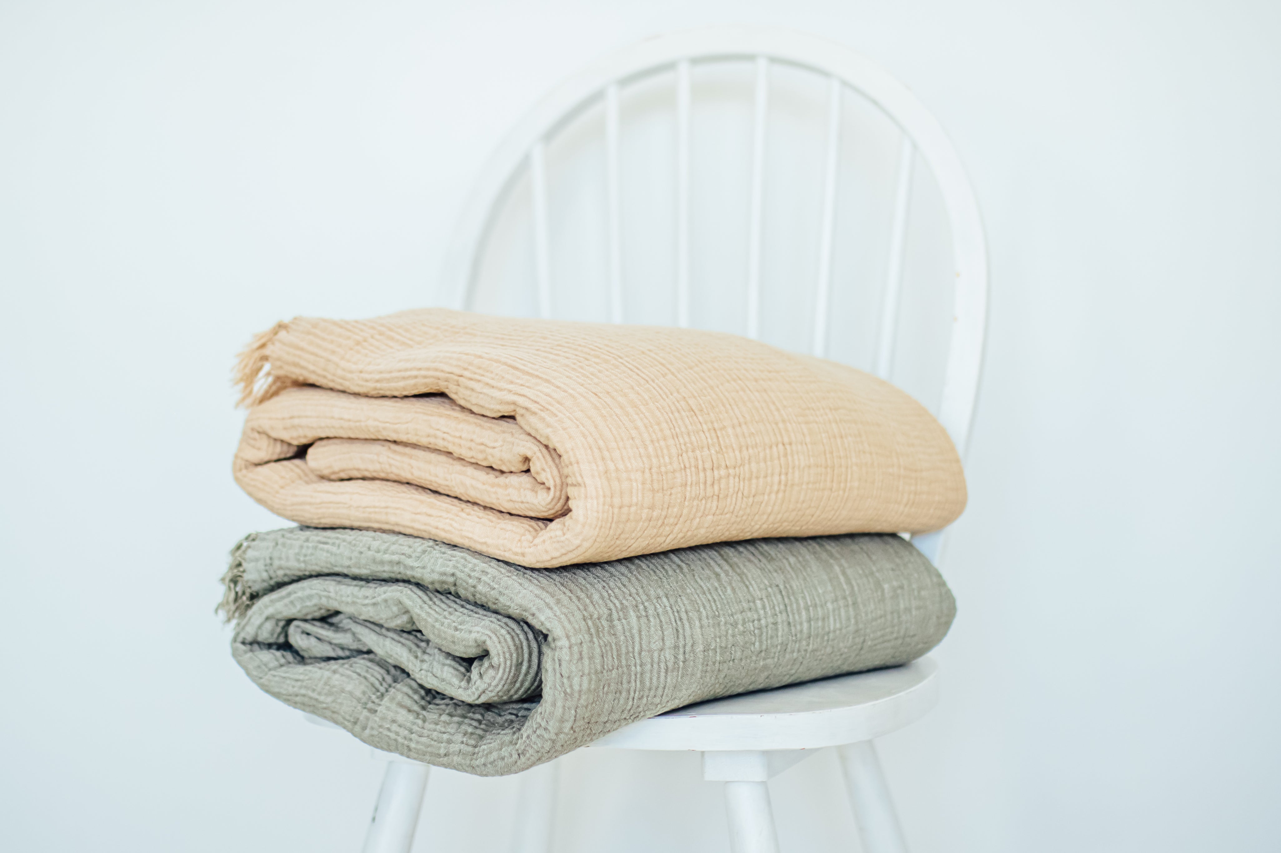 the mustard and sage coloured bed and couch throw blankets folded on a while chair