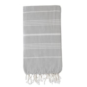 A folded pale grey Turkish towel with white stripes and tassels on the bottom edge.